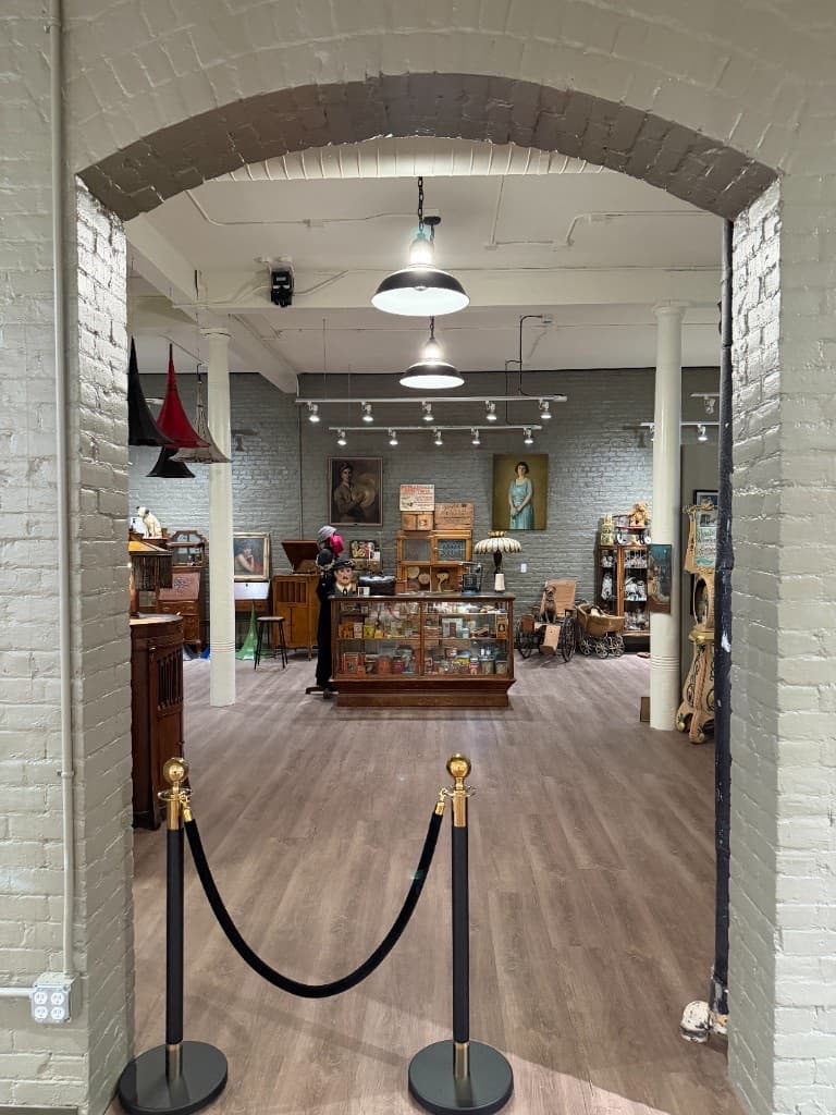 Brick archway framing the main Beautiful Things gallery room, with paintings, display cases, and historic objects beyond.