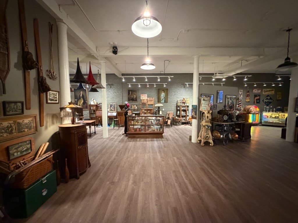 Long view across the Beautiful Things gallery with paintings, display cases, machines, and glowing jukeboxes.