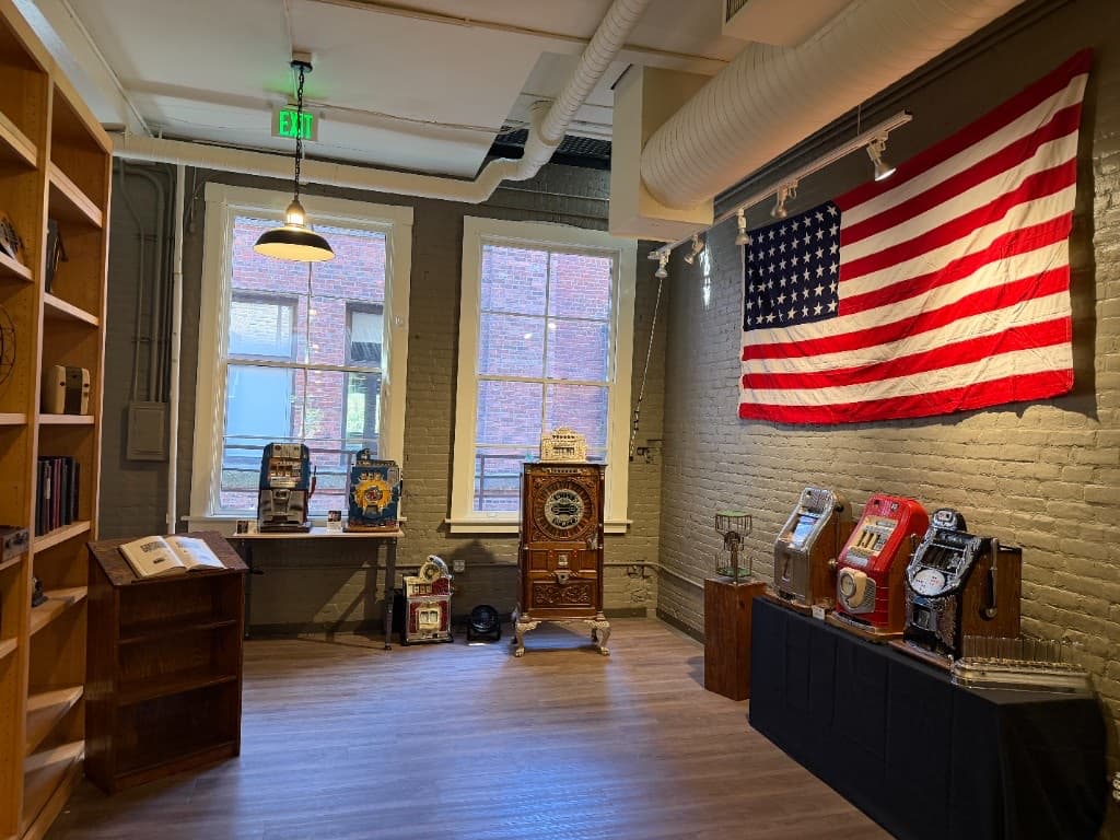 Vintage slot machines and coin-operated amusements displayed beneath a large historic American flag.