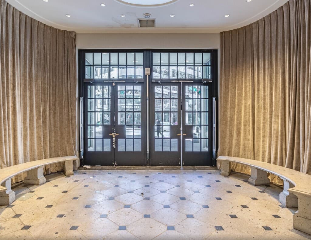 Black-framed glass entry doors inside the Coliseum, flanked by curved benches and draped side walls